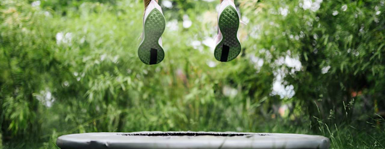 Beine beim Hochspringen auf einem Trampolin im Grünen.
