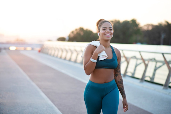 Junge Frau geht morgens entspannt und zufrieden über eine große Brücke, nachdem sie joggen war.