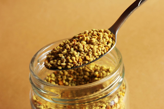 Aus einem Glas wird Blütenpollen mit einem Löffel entnommen.