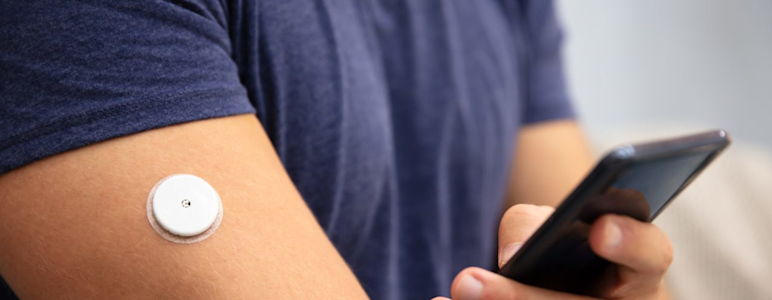 Auf dem Oberarm eines Mannes klebt ein Messgerät, welches auf dem Smartphone den Blutzuckerspiegel zeigen kann.