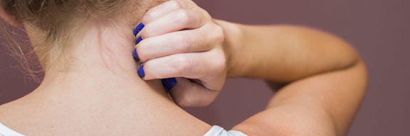 Frau kratz sich im Nacken. Jucken und Rötungen können durch Neurodermitis verursacht werden.