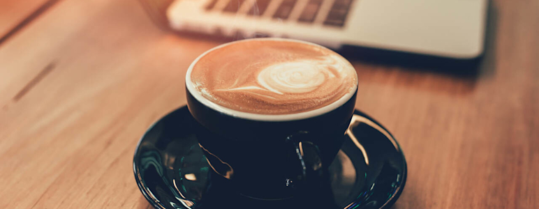 Tasse mit Kaffee neben einem Laptop auf einem Holztisch.
