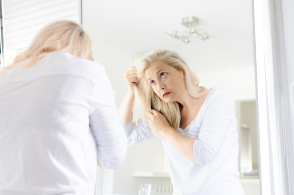 Ältere Frau schaut in den Spiegel, graue Haare, Haarausfall in den Wechseljahren.