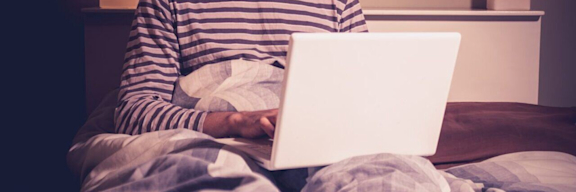 Glücklicher Mann mit Laptop im Bett.