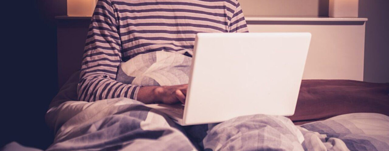 Glücklicher Mann mit Laptop im Bett.
