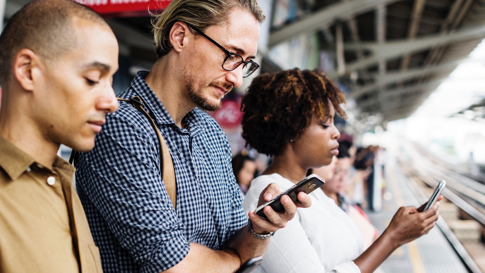 People waiting for train, reading on their phone