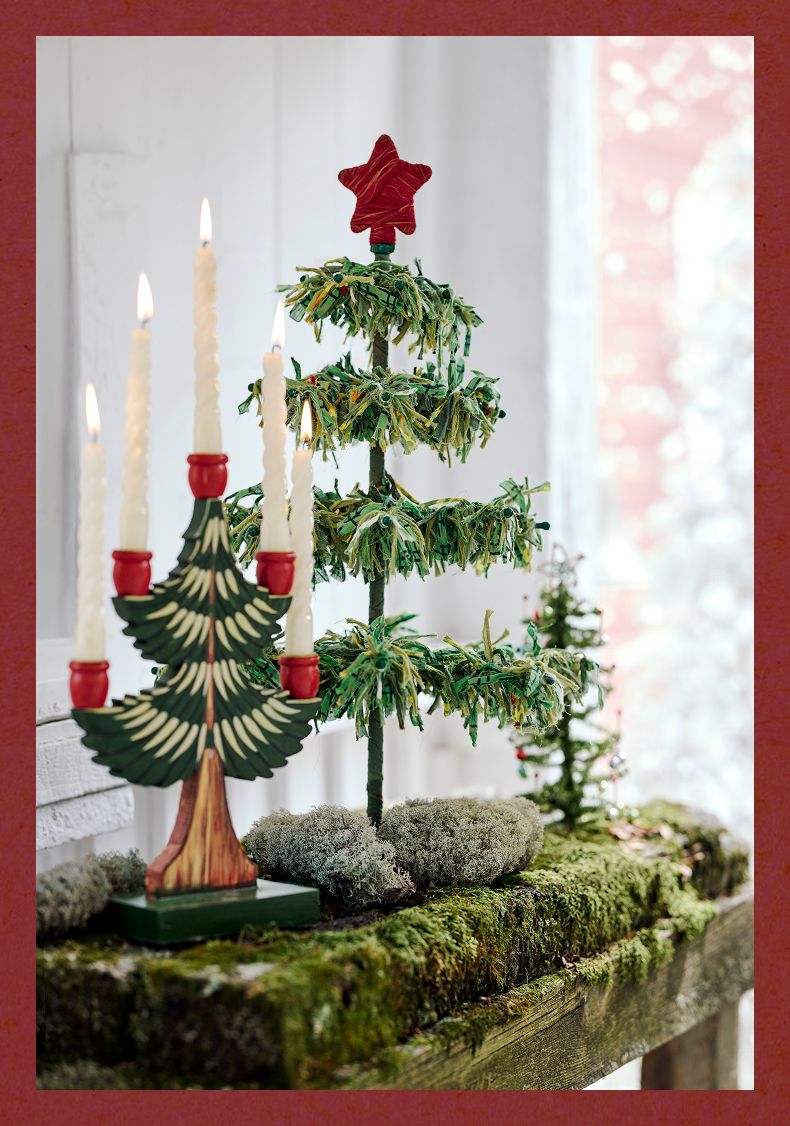 Decorative Christmas tree candelabra with lit candles beside a tiered green tinsel tree topped with a red star.