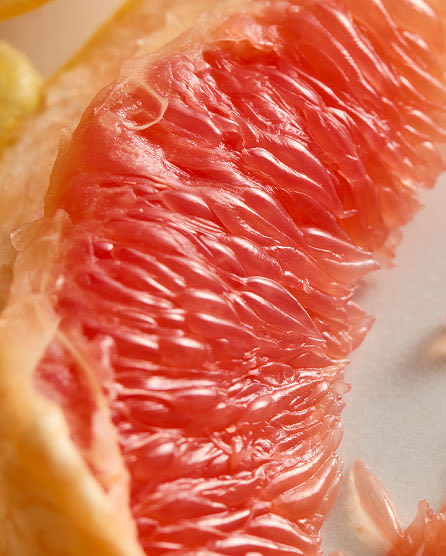 Close-up of pink grapefruit segments showing juicy flesh and translucent membranes with yellow peel visible at edges.