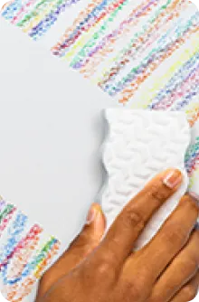 Main utilisant une éponge blanche pour effacer des marques de crayons de couleur sur un mur blanc.