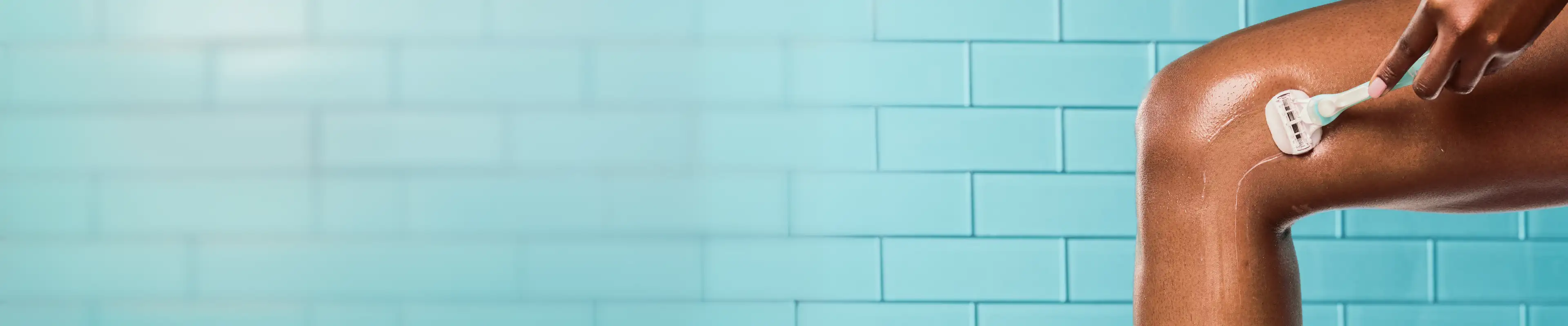 Woman using a razor to shave a lower leg against a tiled background