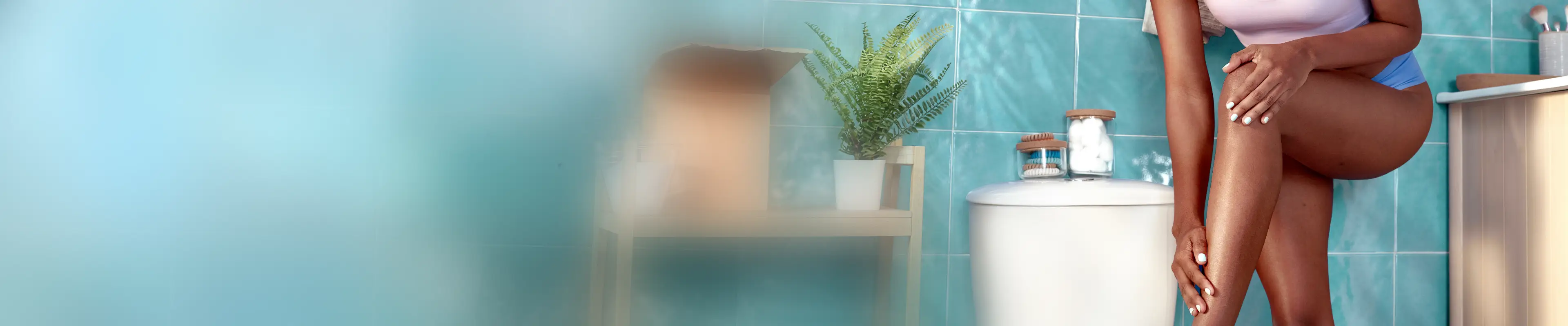 Femme avec les cheveux en chignon, assise sur une baignoire, se rasant la jambe droite.