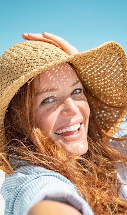Femme souriante portant un chapeau sous un ciel clair