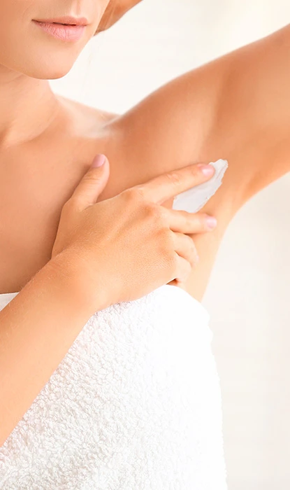 Woman wearing a towel putting cream on her underarm