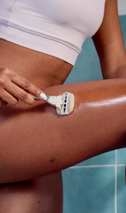 Close up shot of a hand using Gillette Venus pink razor to shave calve