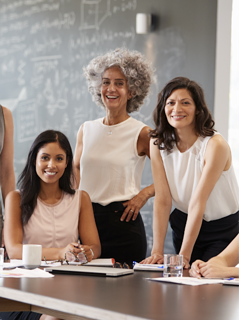 Three women sit and stand around a table at their workplace