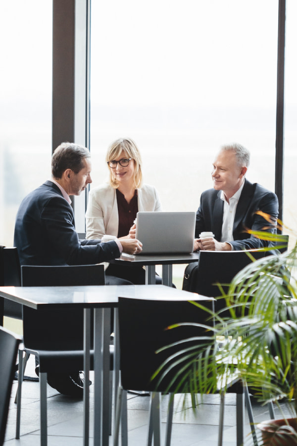 Three people sitting at a table in an atrium setting with plants