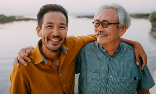 Smiling senior father and adult son on beach