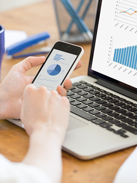 Financial advisor reviewing pie chart on a cell phone in front of a laptop displaying charts.