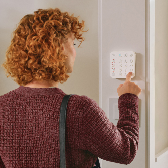Inside Home Basic Kit PDP Ring Alarm. Designed to deter. Ready to respond. Woman stares at Ring alarm keypad.