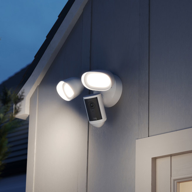 White Floodlight Cam Pro (2nd Gen) at night mounted to the side of a home, both floodlights shining.