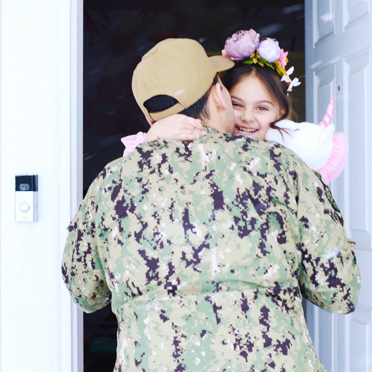 Man in military uniform hugs young girl dressed as princess in doorway of home, with Ring Video Doorbell mounted on wall.