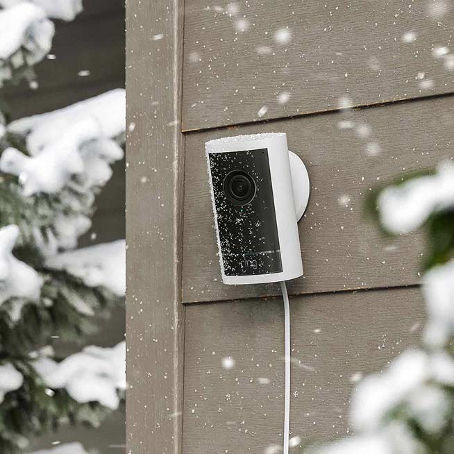White Outdoor Cam Pro in the snow mounted to the side of a home.