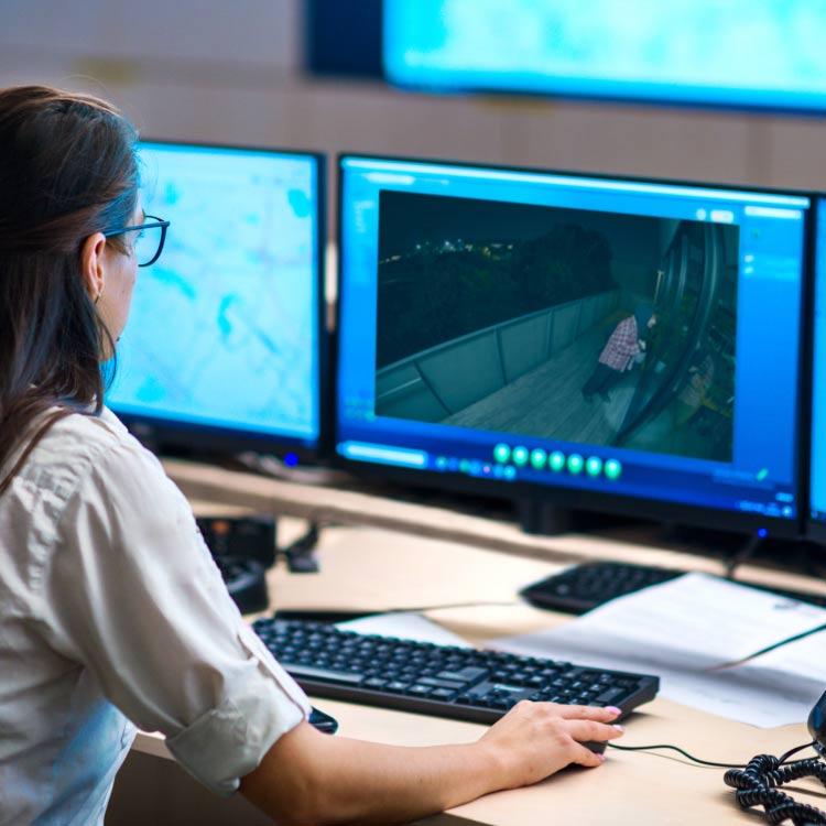 A woman sits at a desk monitoring two computer screens.