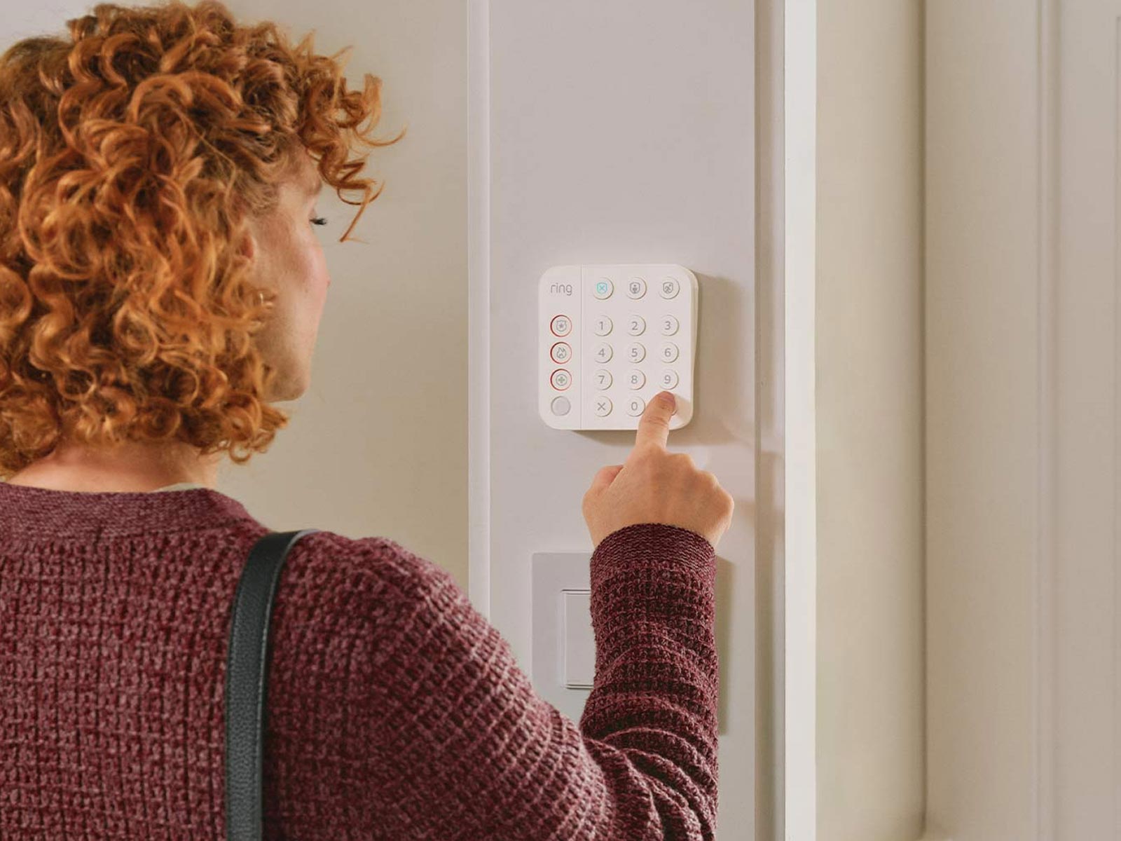 Person using wall-mounted Ring Alarm Keypad, with living room in background.