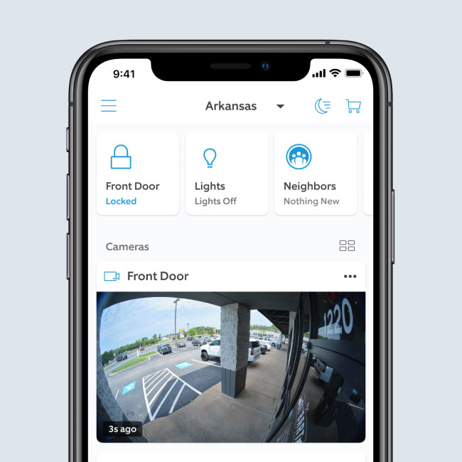 A smartphone screen displaying the Ring App's business security dashboard, showing a live front-door camera feed of a business parking lot, door lock status, and device controls.