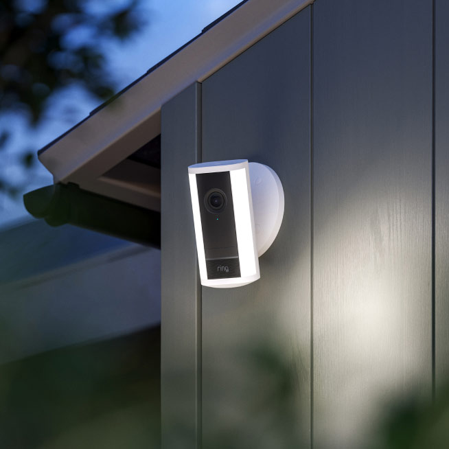 White Spotlight Cam Pro (2nd Gen) at night mounted to the side of a home, LED spotlights shining.