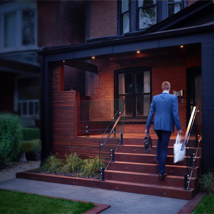 Man returning home at dusk to an illuminated porch.