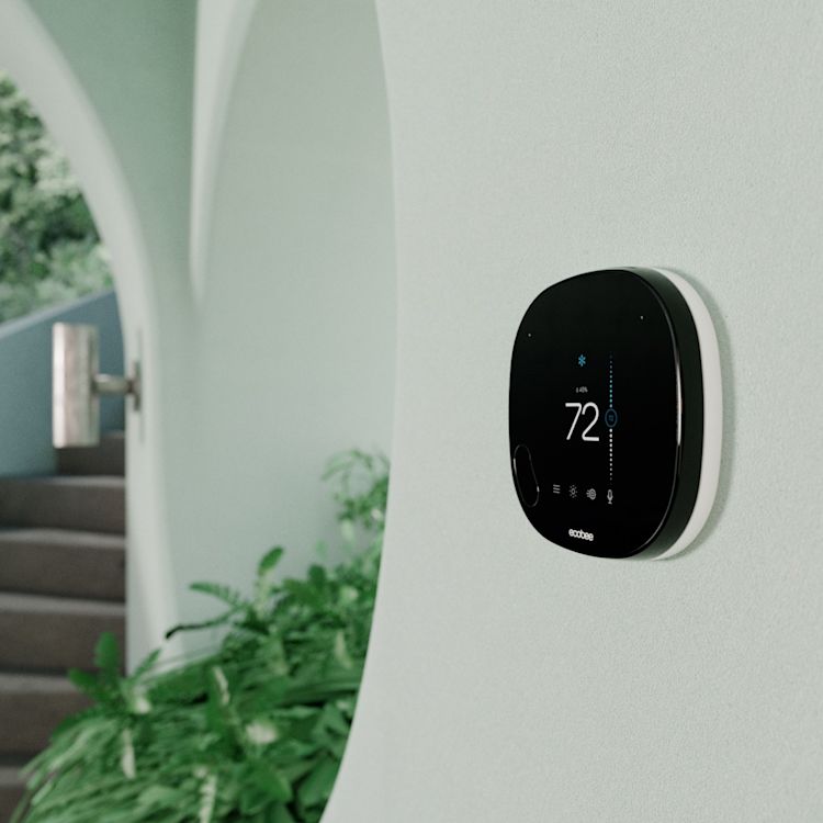 SmartThermostat with Voice mounted on wall, with plants in the background