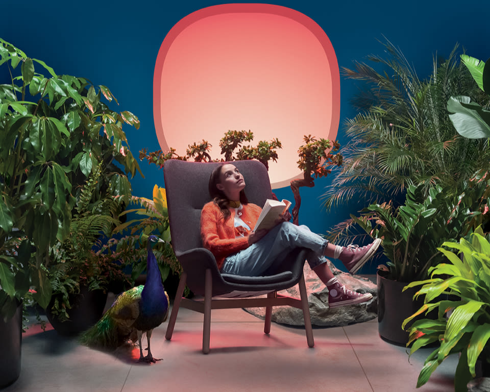 A woman sits on a chair in the middle of a plant-filled room.