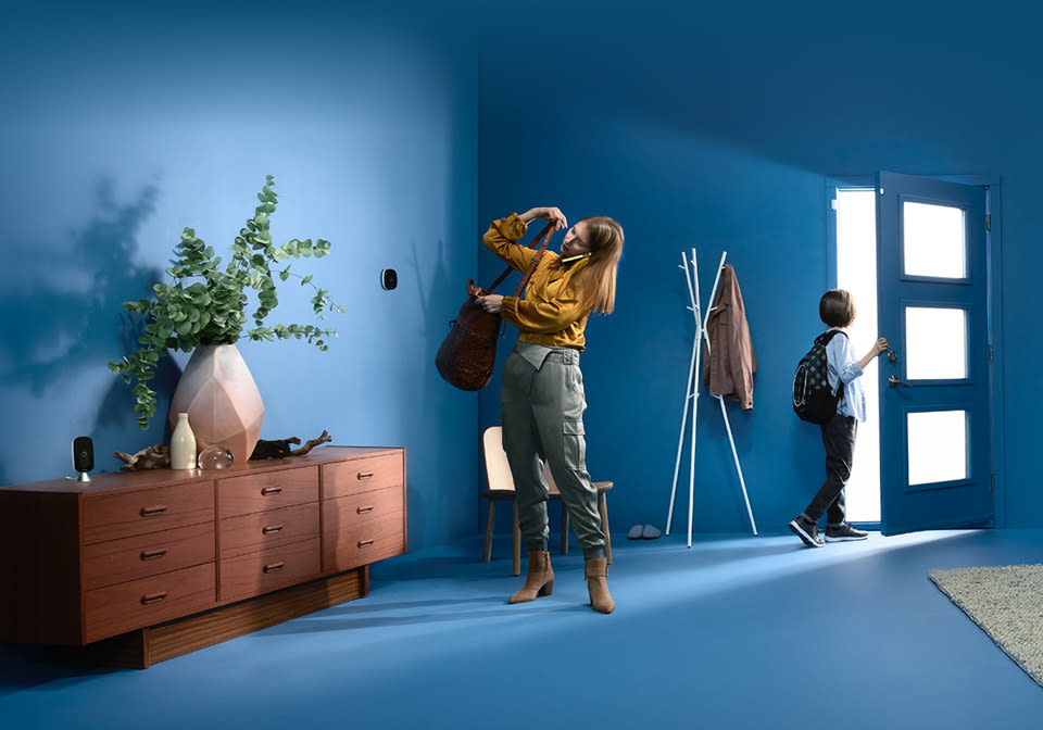 A woman and child get ready to leave a house, with an ecobee thermostat and camera also in frame.
