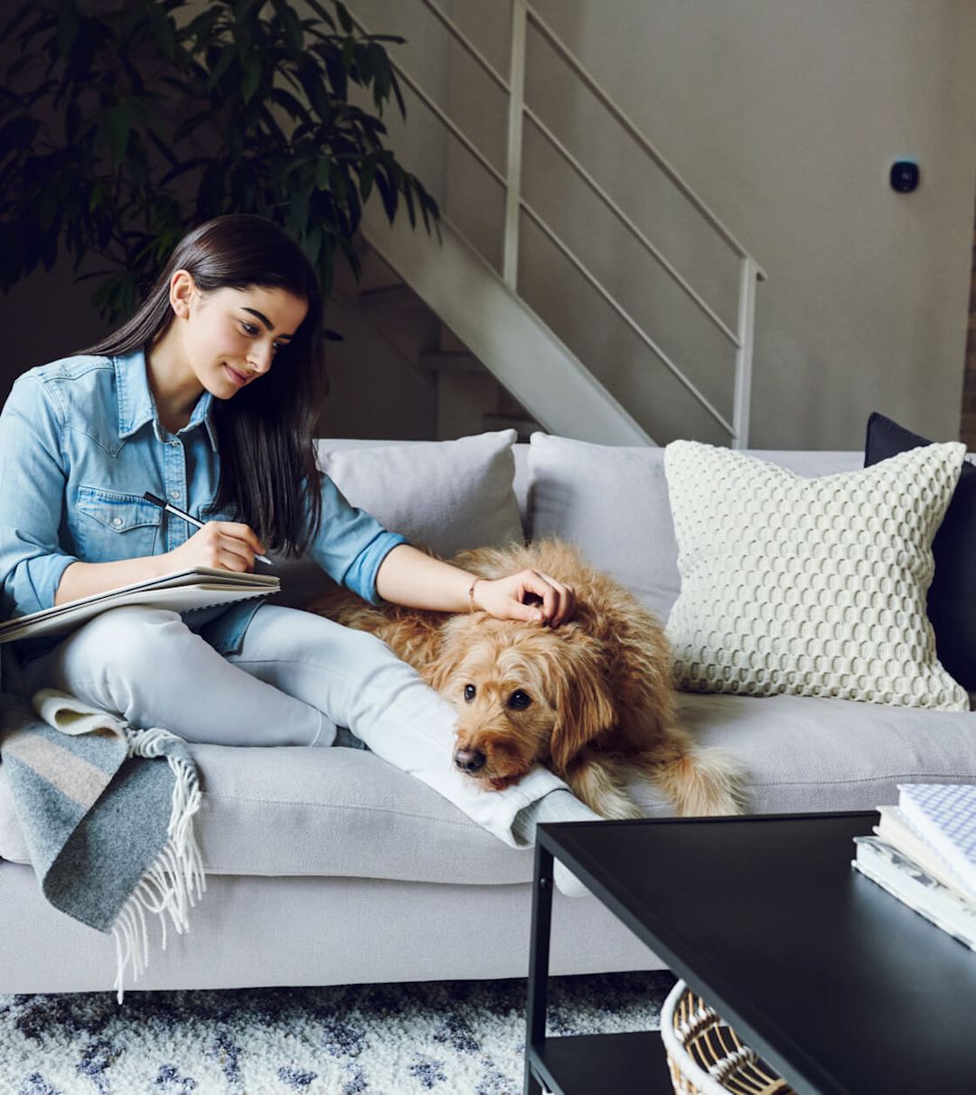 A woman sits on a couch with a dog; an ecobee thermostat is on the wall in the background.