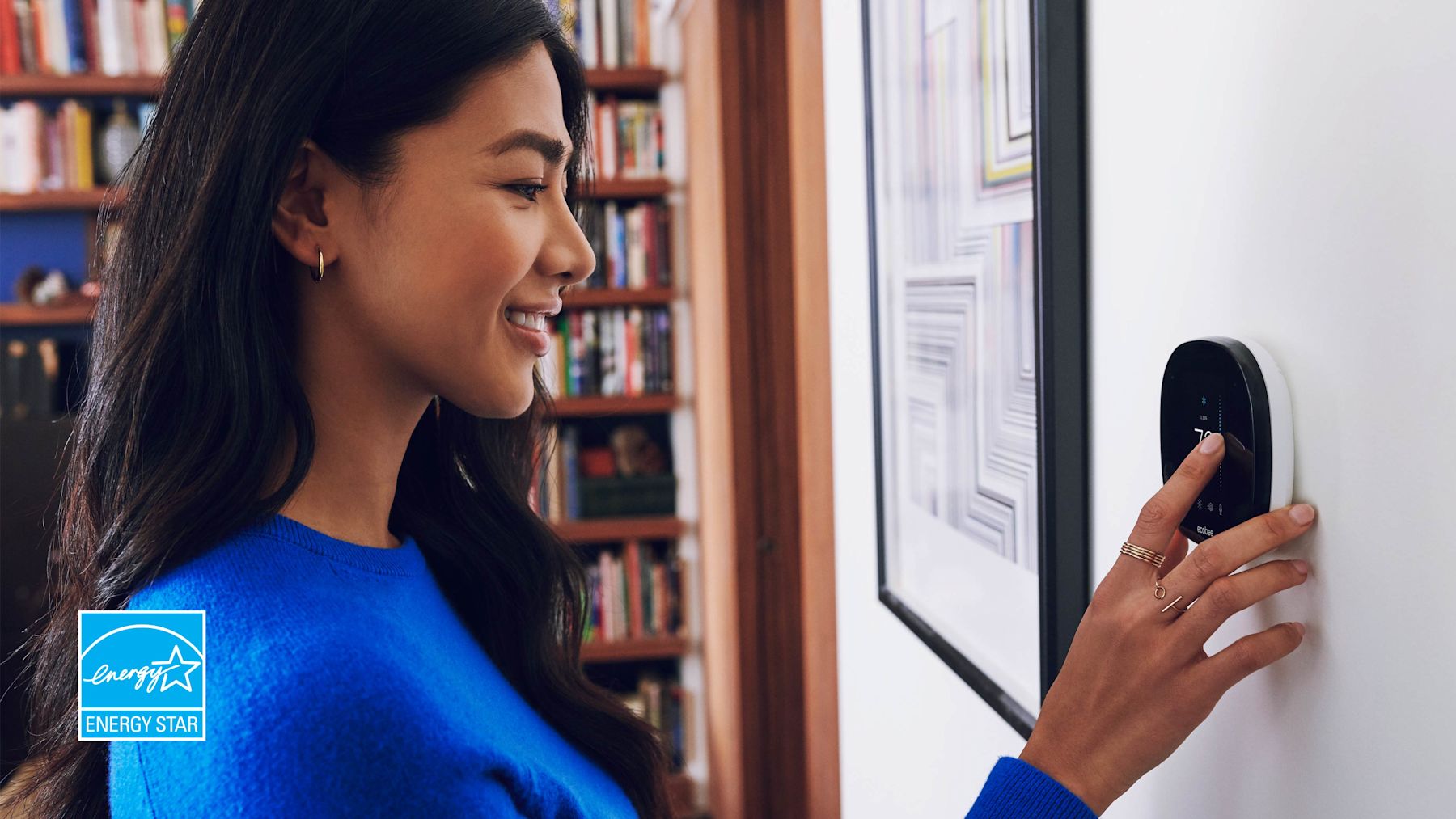 Woman in blue top adjusting thermostat.
