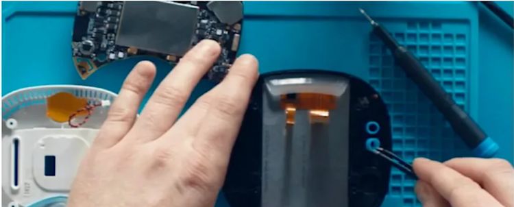 A top-down shot of a person working on a partially disassembled ecboee thermostat. The person is attaching a small blue piece of plastic to the thermostat with tweezers.