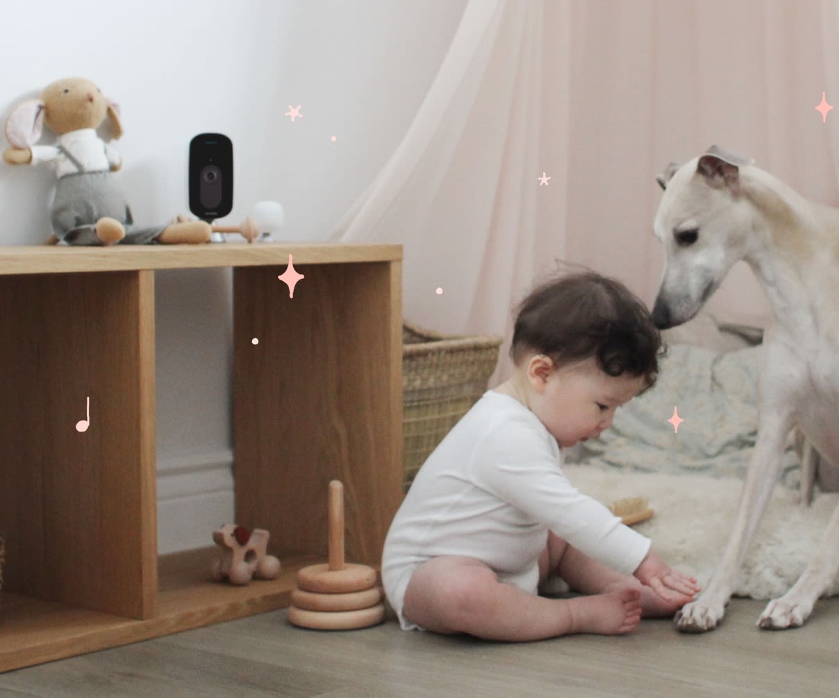 A baby plays on the floor with a dog while the ecobee SmartCamera monitors from a shelf.
