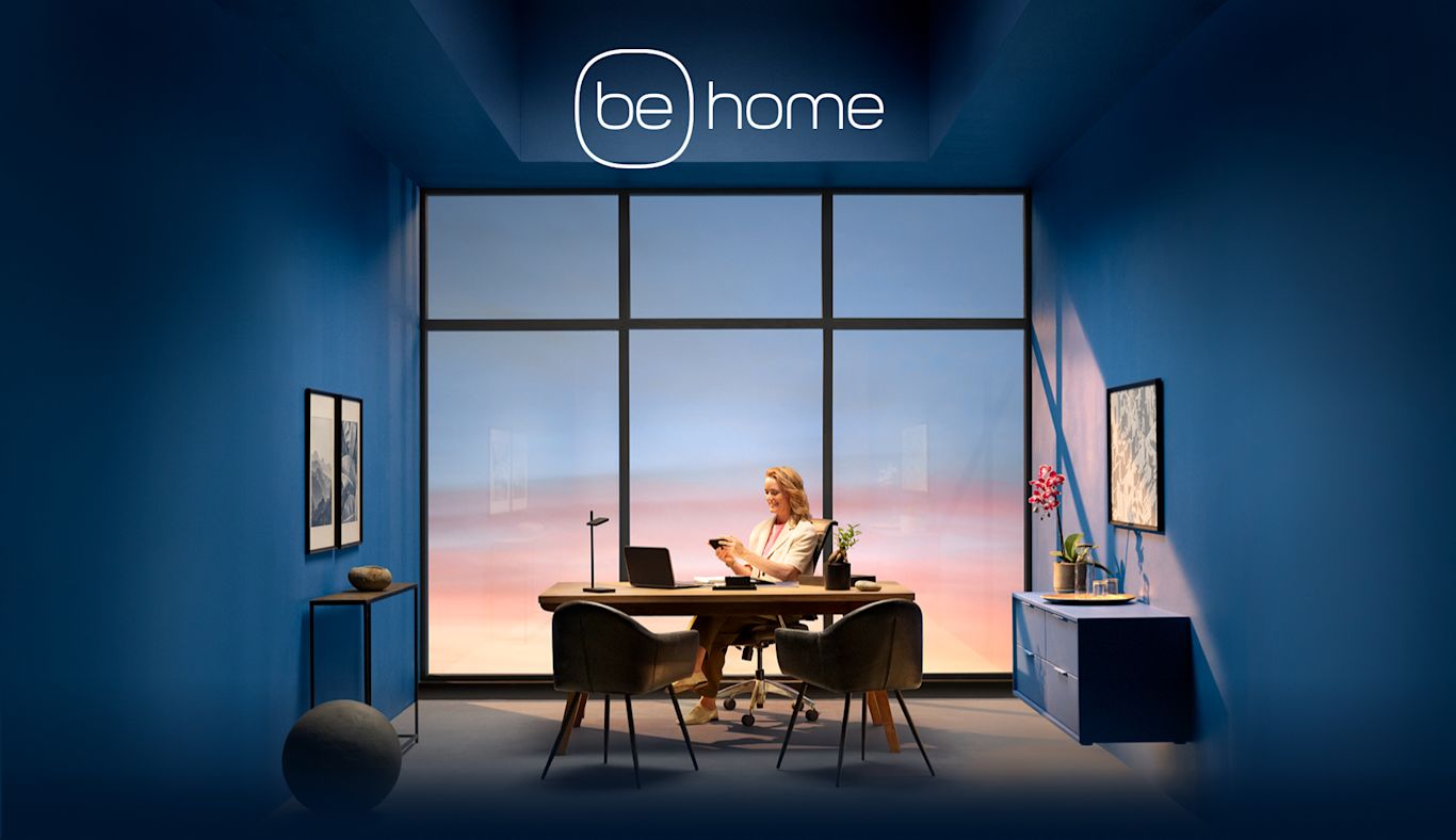 A woman sits looks at her phone while sitting in an office. Text saying "be home" floats above her.