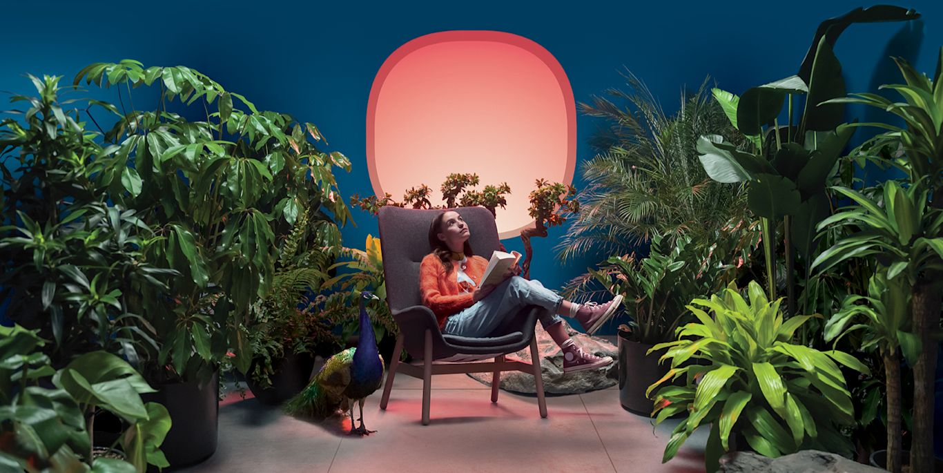 A woman sits on a chair in the middle of a plant-filled room.