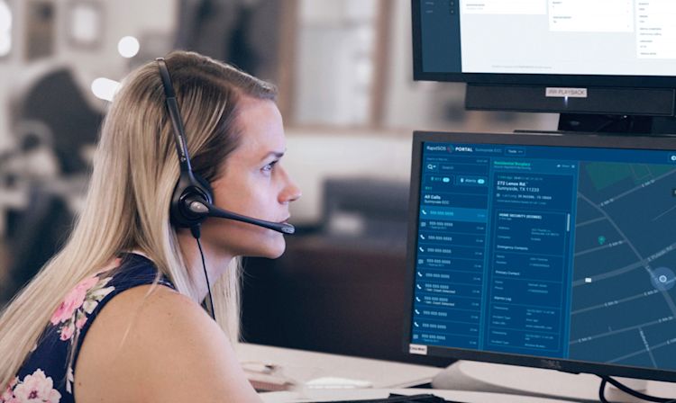 A woman sits in front of a computer screen wearing a headset; the screen shows a map.