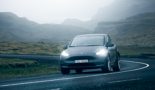A sleek gray Tesla car traverses a winding road with a backdrop of foggy, mountainous terrain, highlighting the blend of modern technology with rugged nature