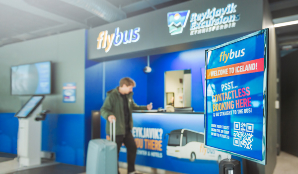 A traveler interacts with frint desk agent at the Flybus service area, preparing for transport from Keflavík Airport to Reykjavík.