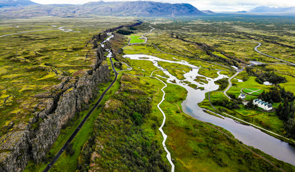Aerial view of a winding river through a lush, expansive valley with rocky cliffs.