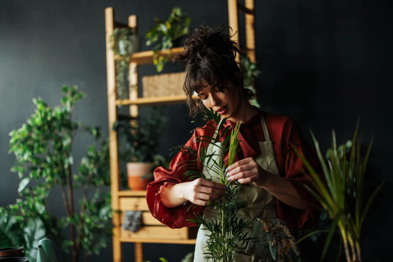 Young woman wearing an apron taking care of her plants in a modern room with dark walls