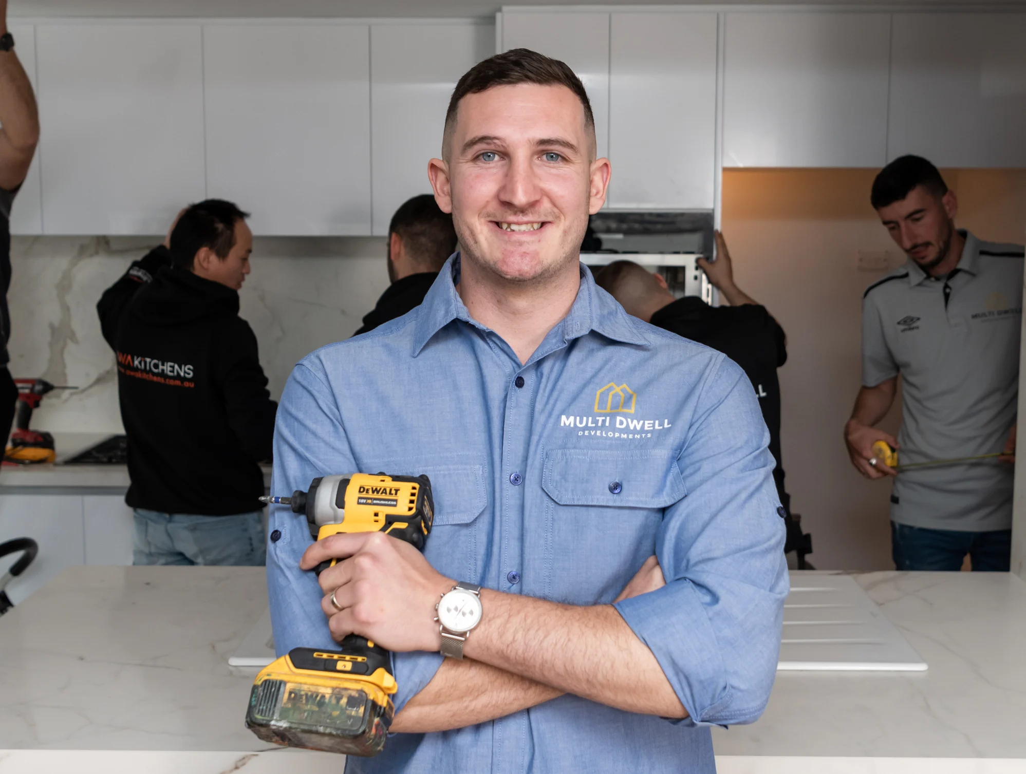 Jason Samargis, owner of Multi Dwell Developments, stands in a kitchen on a worksite. He has a big smile on his face and is holding a DeWalt drill.