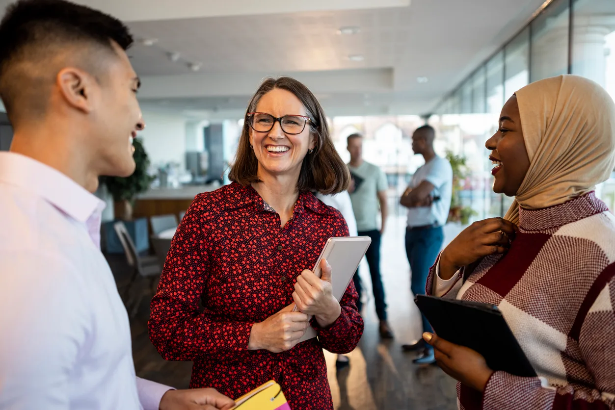 Three employees gather in an office, smiling and chatting