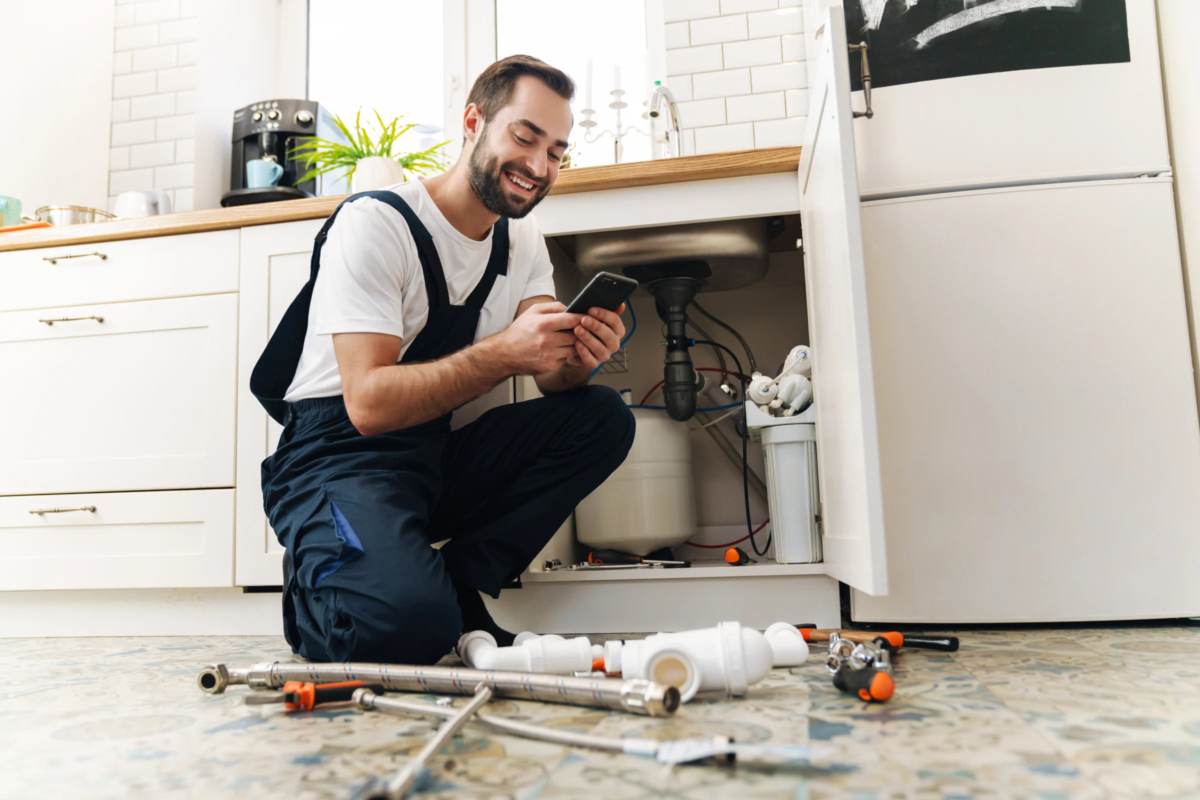 A lifestyle image of a plumber smiling while looking at his phone in front of a sink.