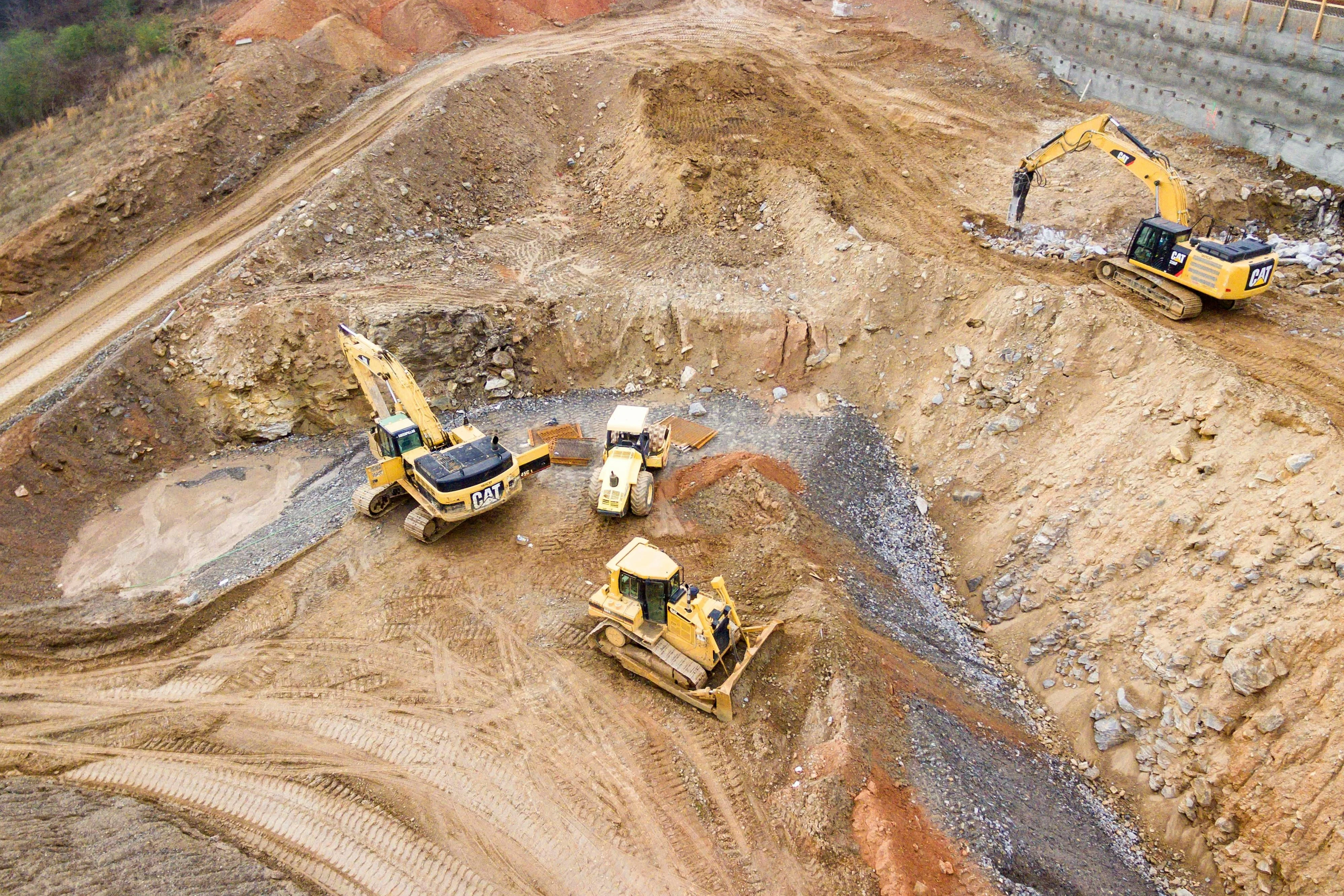 Aerial view of a large construction site with yellow CAT excavators and a bulldozer moving earth and gravel.