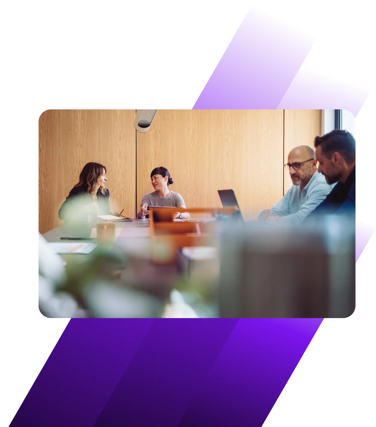 Diverse professionals in a modern meeting room with wooden walls, collaborating around a conference table with laptops.